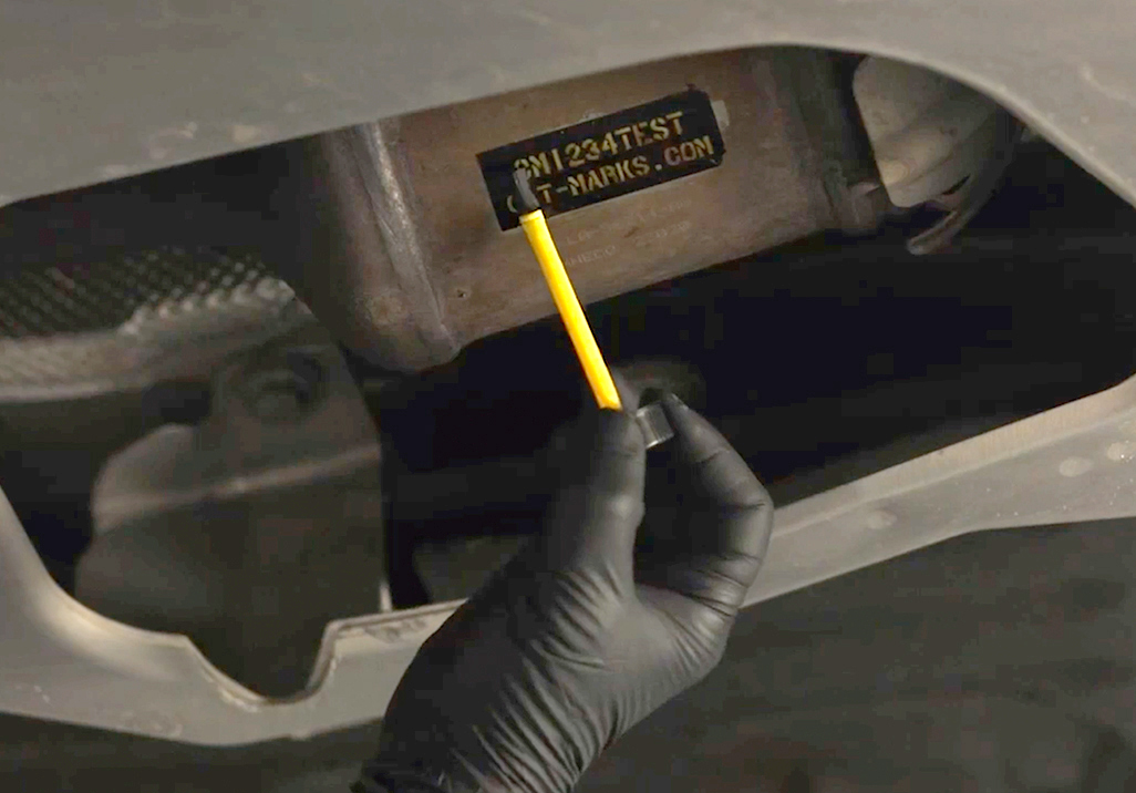 Applicator brush next to a stencil attached to a catalytic converter.